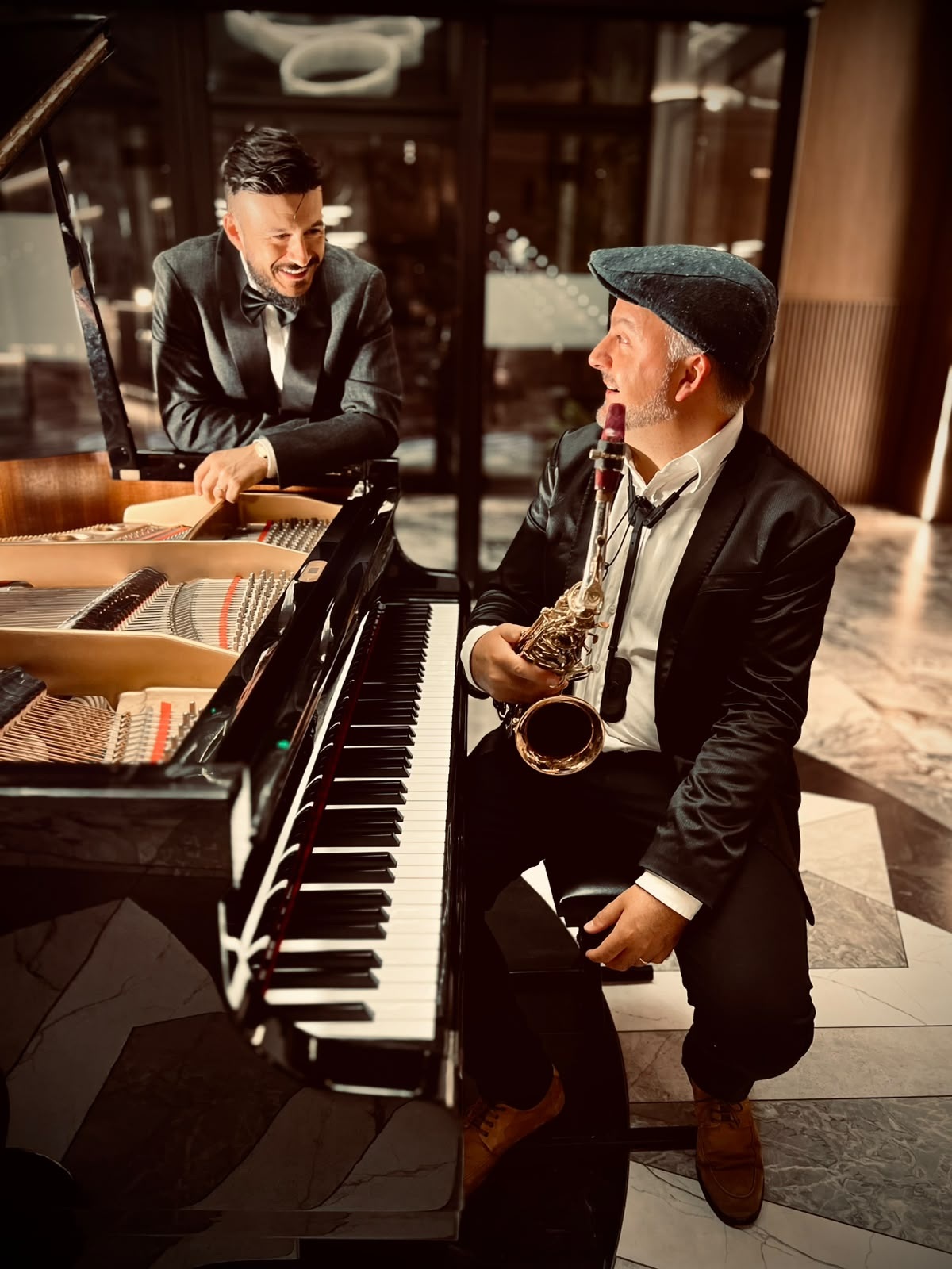 Elvis Claro e Giovani Tramontin sorridono accanto al pianoforte a coda, con il sassofono