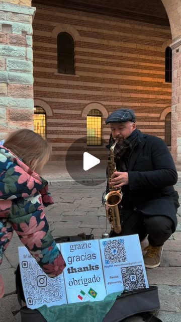 Giovani Tramontin suona il sax contralto in un centro storico, con un cartello di ringraziamento in più lingue